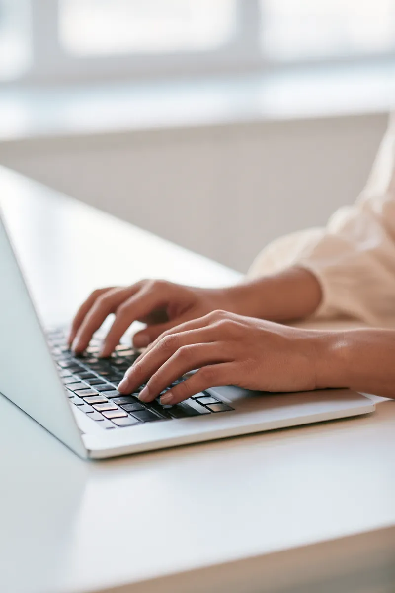 Hands typing on a slim laptop on a white desk while completing a personal loan request form
