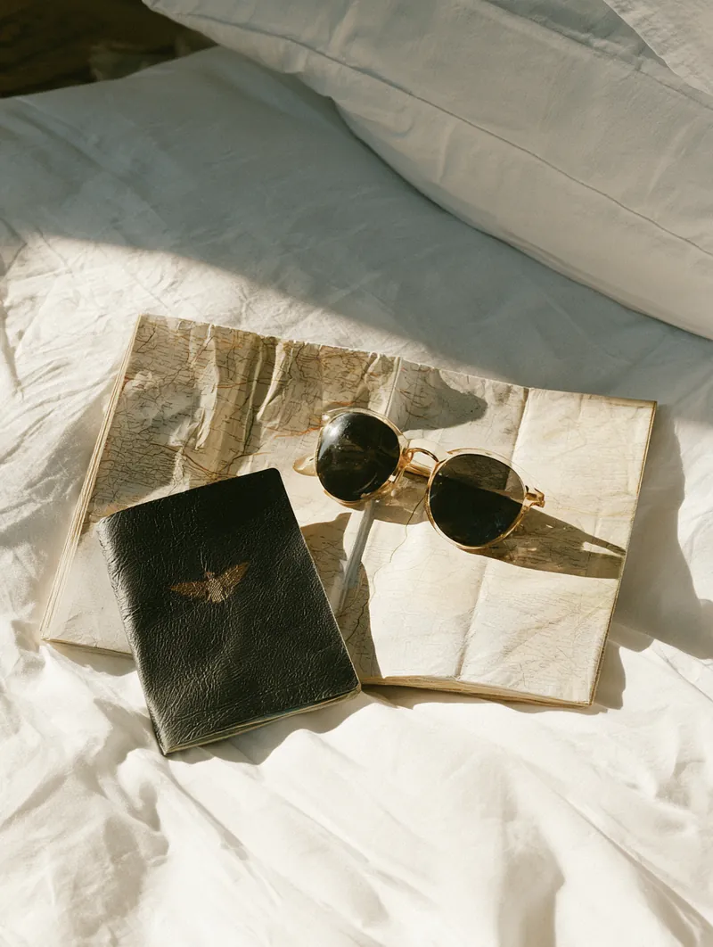 Passport, sunglasses and a folded map lying on white hotel bedding