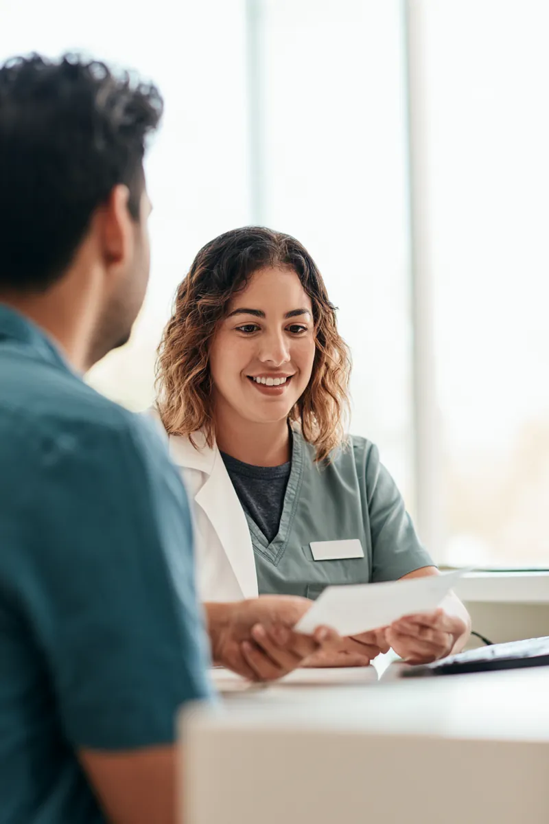 Clinic billing coordinator explaining payment options to a man in his thirties at a reception desk